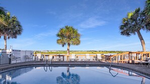 A pool area with lounge chairs, a palm tree, and a view of the landscape.