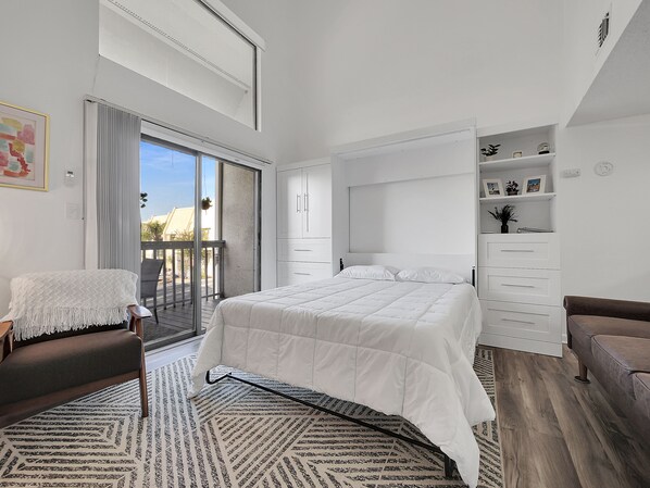 Une chambre à coucher comprenant un lit, une chaise, un canapé, une grande fenêtre et un balcon.