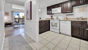 A modern kitchen with dark wooden cabinets, white appliances, and a tiled floor.