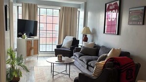 Una sala de estar con sofá, sillones, una mesa de centro, televisor y una ventana con cortinas.