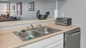 Una cocina con armarios blancos, un lavamanos doble, un tostador y un lavavajillas.