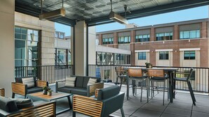 An outdoor seating area with modern furniture, a view of a brick building, and a balcony railing.