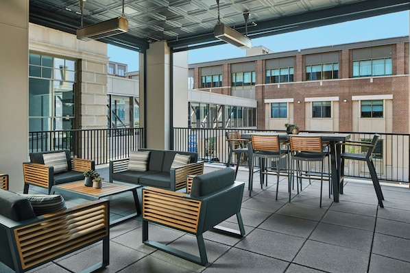 An outdoor seating area with modern furniture, a view of a brick building, and a balcony railing. - The Olive Ann Hotel, Grand Forks, a Tribute Portfolio Hotel (Grand Forks)