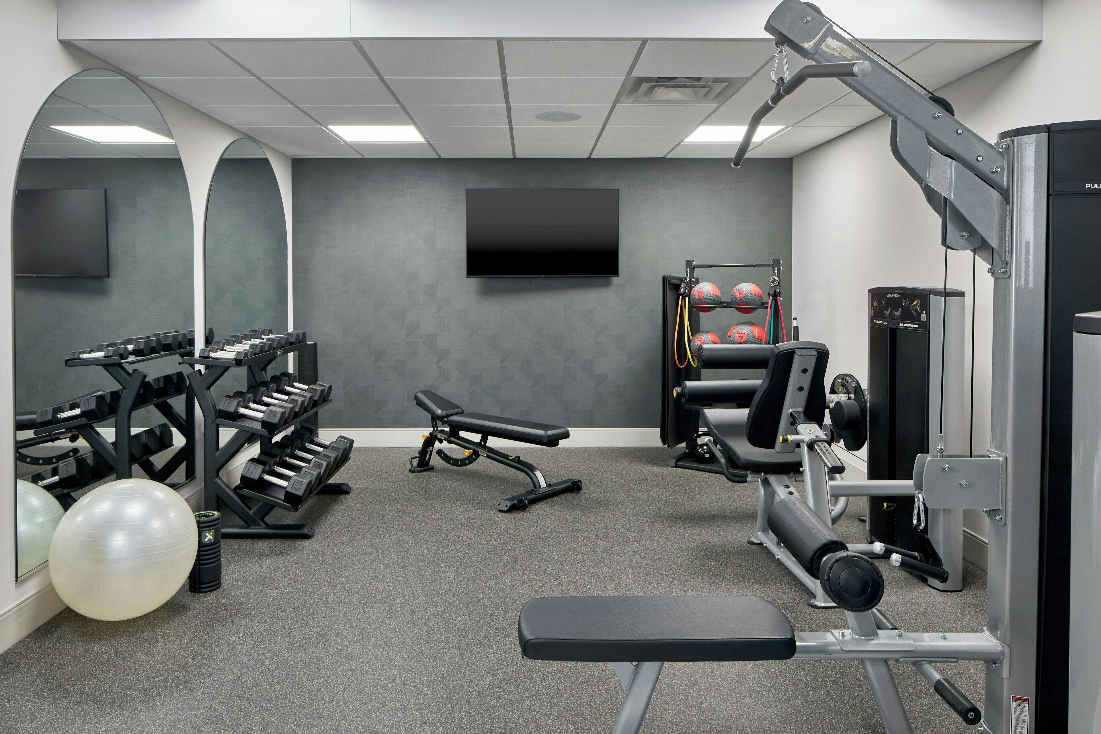 A gym with exercise equipment, a bench, and a TV mounted on the wall.