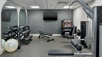 A gym with exercise equipment, a bench, and a TV mounted on the wall.