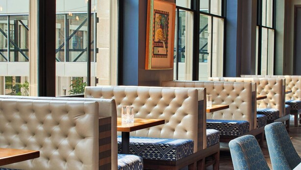A restaurant interior with high ceilings, exposed ductwork, and hanging pendant lights.