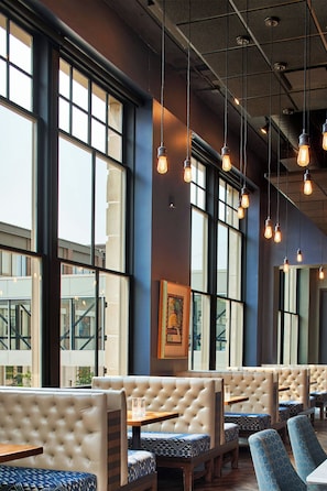 A restaurant interior with high ceilings, exposed ductwork, and hanging pendant lights. - The Olive Ann Hotel, Grand Forks, a Tribute Portfolio Hotel (Grand Forks)