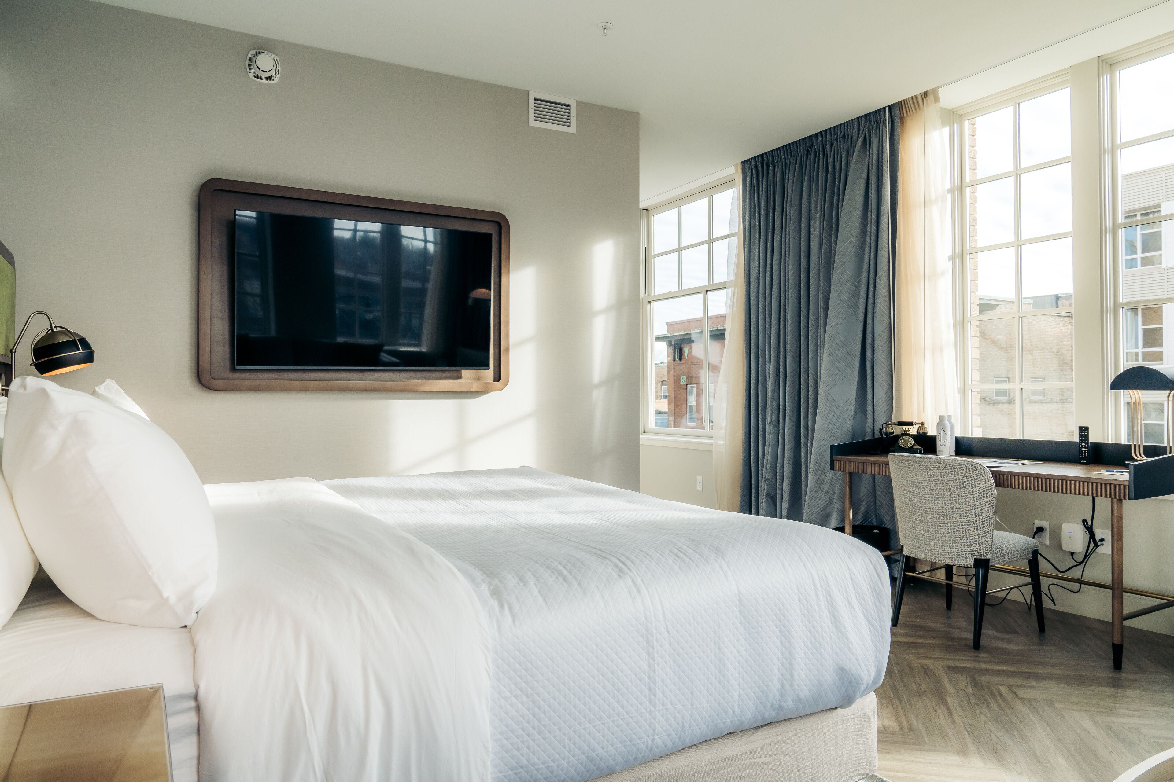 A modern hotel room with a large bed, a desk, and a chair.