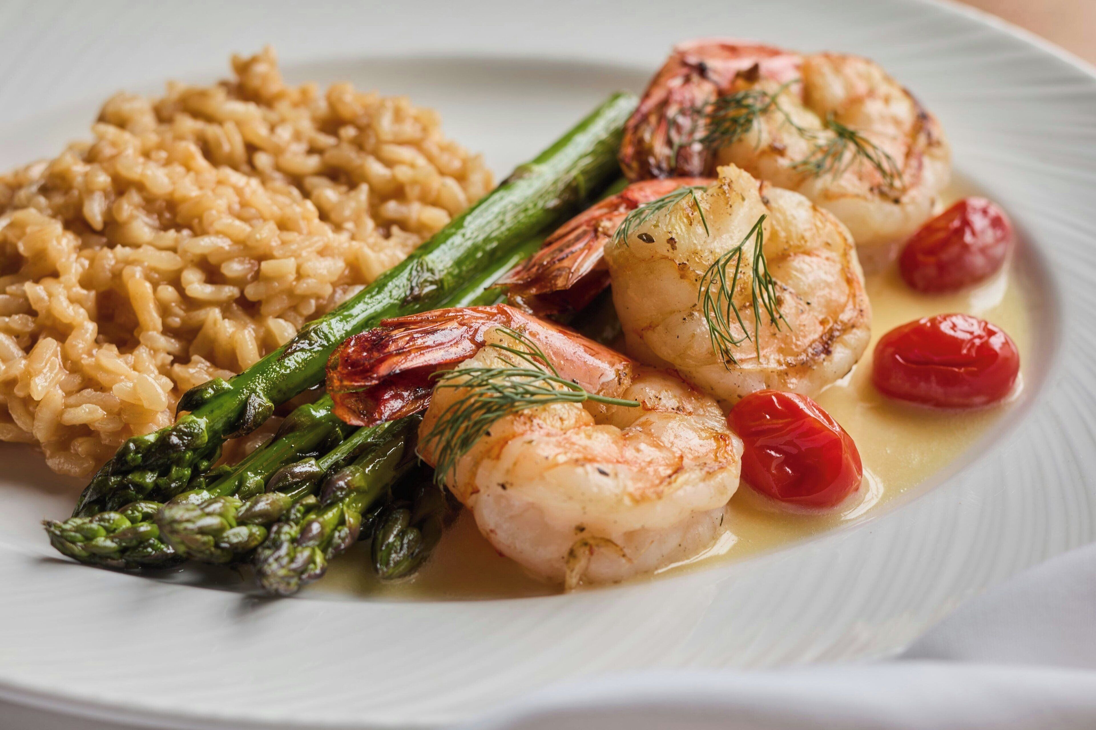 A plate of food with shrimp, asparagus, cherry tomatoes, and risotto.