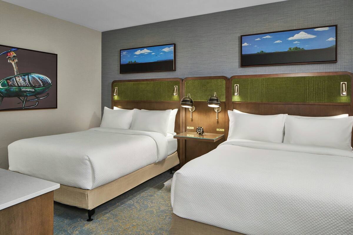 A hotel room with two beds, a small table, and a television on the wall.