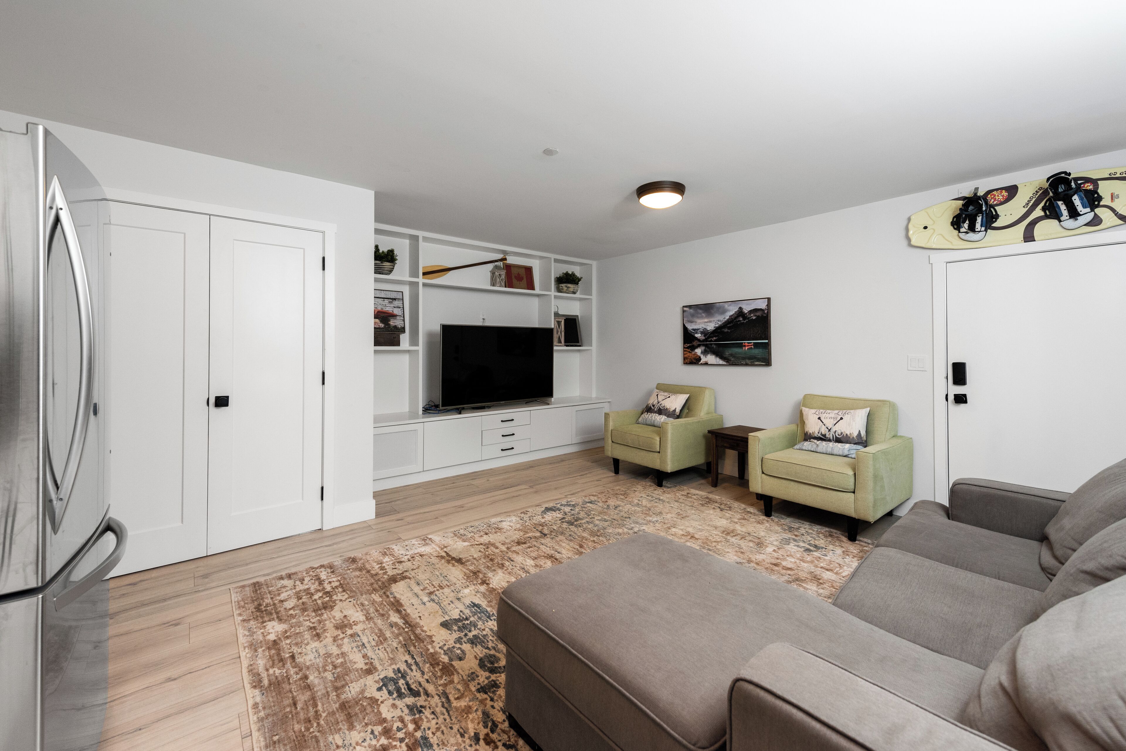 A modern living room with a flat-screen TV, two armchairs, a sofa, a coffee table, and a large rug.