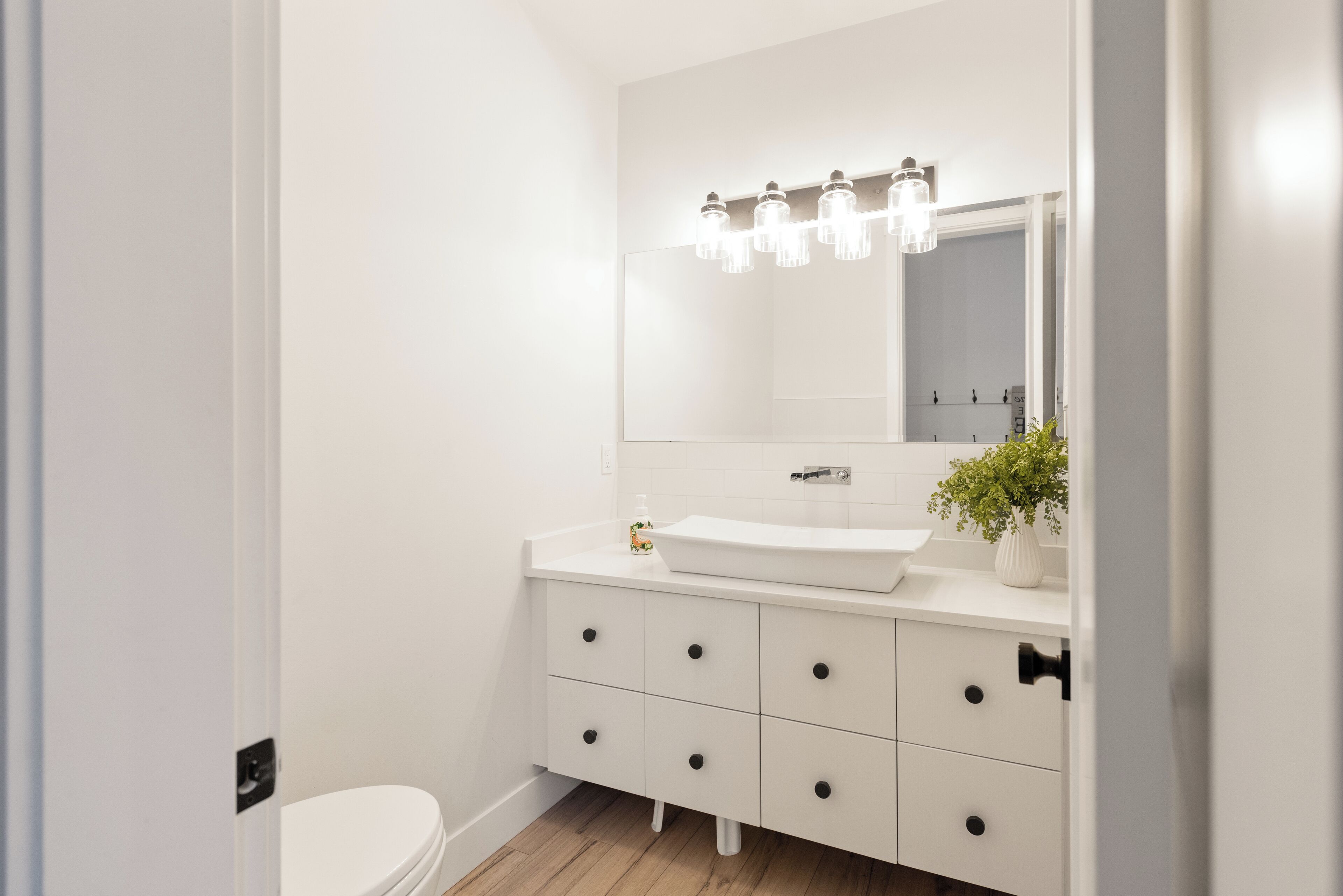 Un baño moderno con un lavamanos blanco, un espejo con iluminación y una planta en maceta.