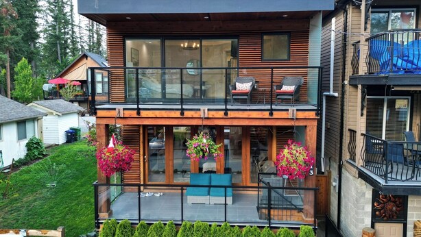 Una casa moderna de dos pisos con balcón, ventanas amplias y un jardín bien cuidado.