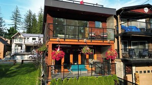 Una casa moderna de dos pisos con un balcón, una bandera y macetas colgantes de flores.
