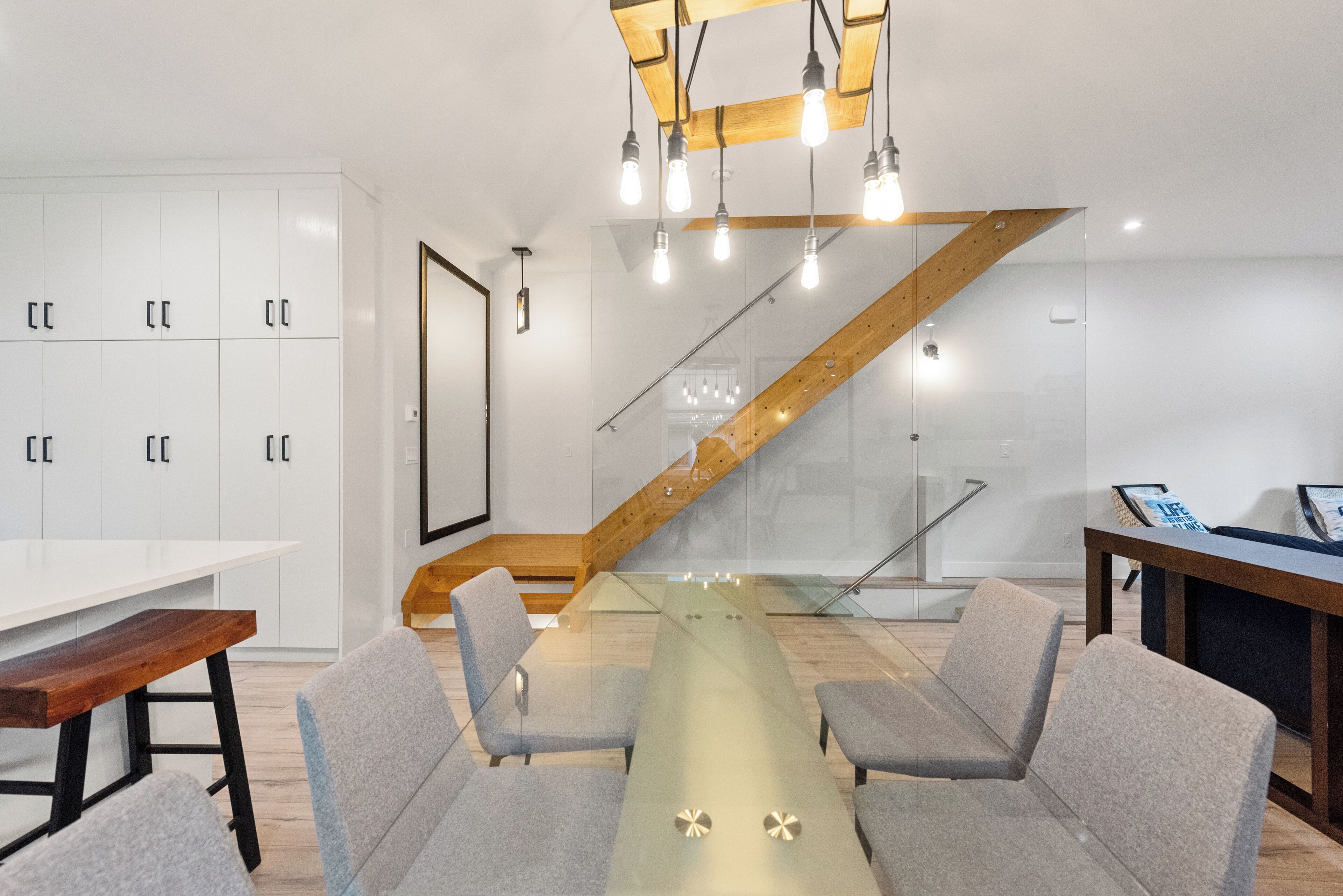 A modern meeting room with a glass table, grey chairs, wooden accents, and a staircase with wooden beams.