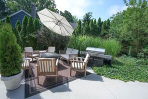 An outdoor patio with a dining set, a grill, and a large umbrella.