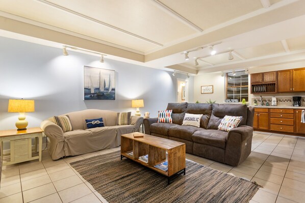 A living room with two sofas, a coffee table, and a kitchen area with wooden cabinets.