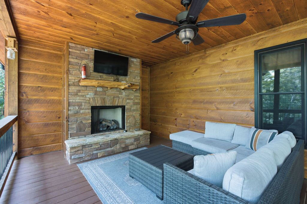 A wooden cabin interior with a stone fireplace, a ceiling fan, and a sofa with cushions.