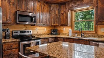 A kitchen with wooden cabinets, stainless steel appliances, granite countertops, and a window with a view of trees.