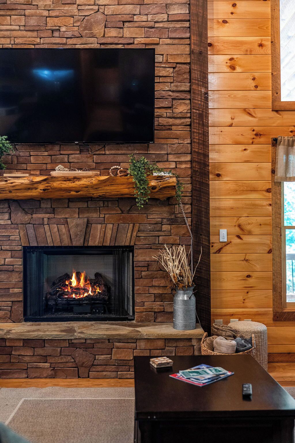 Una chimenea con un televisor encima, un fuste de madera y un jarrón con plantas secas.
