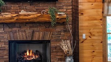 Una chimenea con un televisor encima, un fuste de madera y un jarrón con plantas secas.