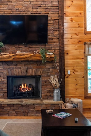 A fireplace with a TV above it, a wooden mantel, and a vase with dried plants. - Sunrays - Hot Tub, Outdoor Fireplace & Game (Morganton)