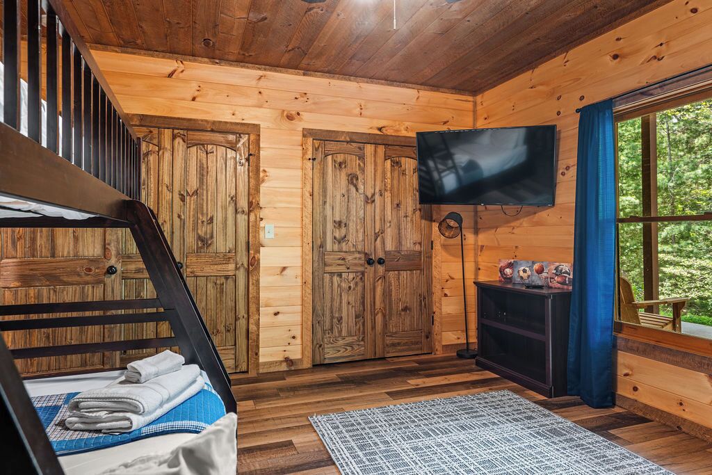 L’intérieur d’un chalet en bois, avec un lit superposé, un téléviseur et une vue sur l’extérieur.