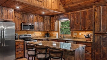 Una cocina con gabinetes de madera, electrodomésticos de acero inoxidable, encimera de granito y una isla central con taburetes de bar.