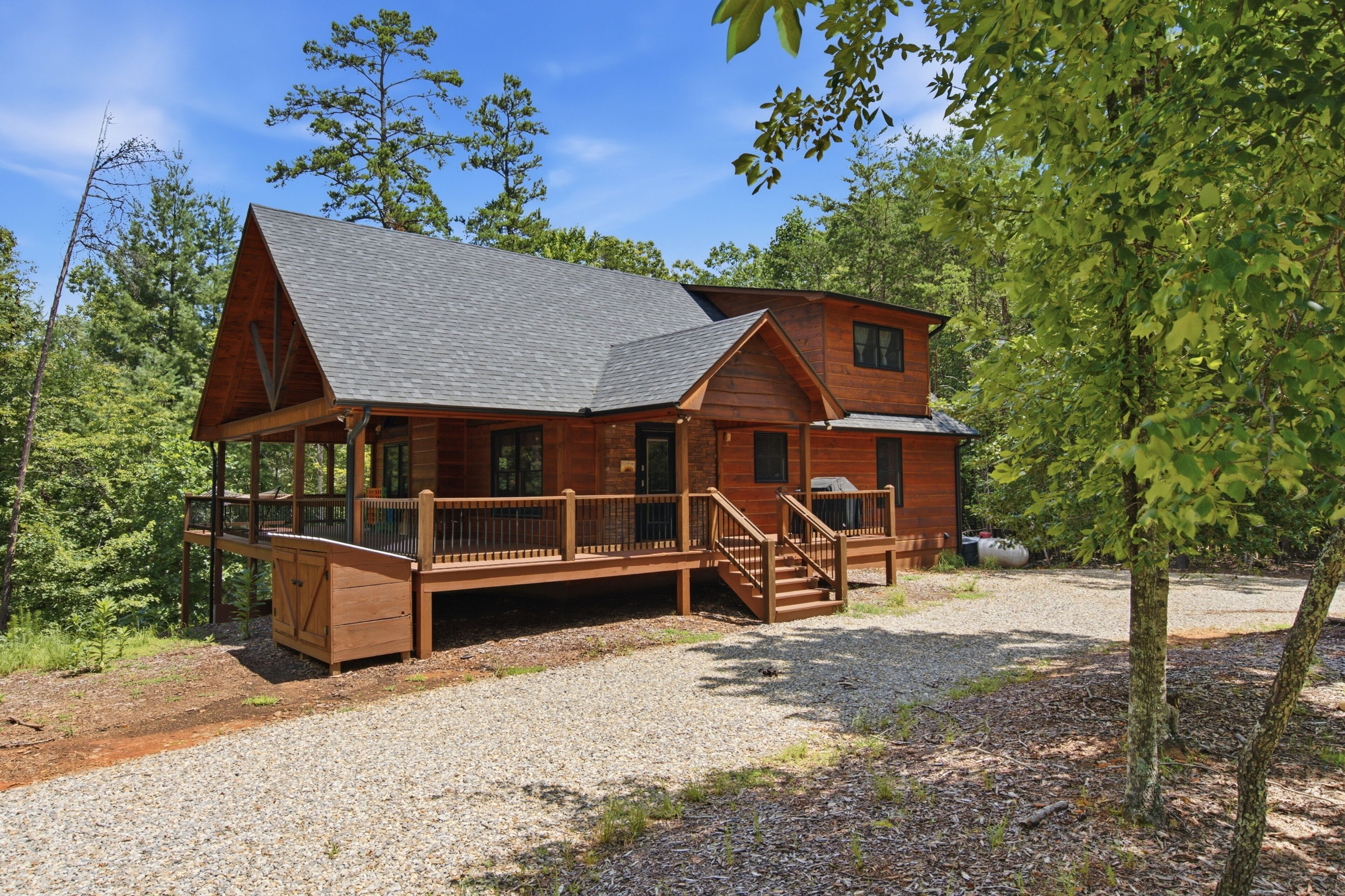 A cabin with a porch, a covered deck, and a gravel driveway.