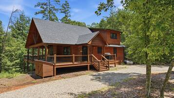 A cabin with a porch, a covered deck, and a gravel driveway.
