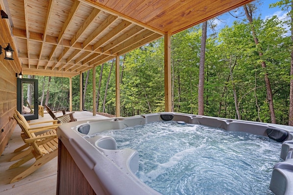 A wooden cabin with a hot tub and wooden chairs.