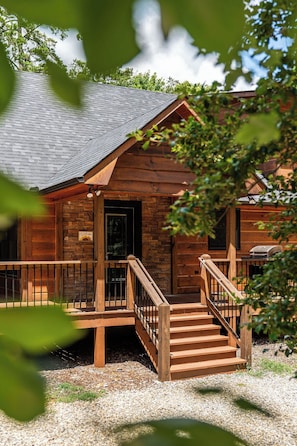 A wooden cabin with a stone fireplace, a wooden porch, and a staircase leading to the entrance. - Sunrays - Hot Tub, Outdoor Fireplace & Game (Morganton)