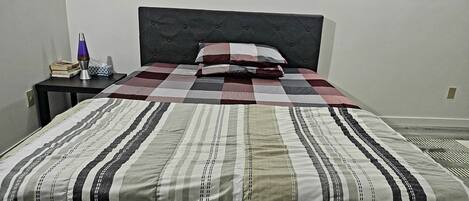A neatly made bed with striped bedding, a dark headboard, and a small bedside table with a lamp and books.