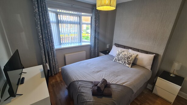 A bedroom with a large bed, a bedside table, a lamp, a radiator, and a window with curtains. - Ravenhill Town house  Belfast (Belfast)