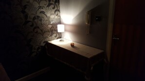 A dimly lit room with a bedside table, a lamp, and a wall with floral wallpaper. - Ravenhill Town house  Belfast (Belfast)