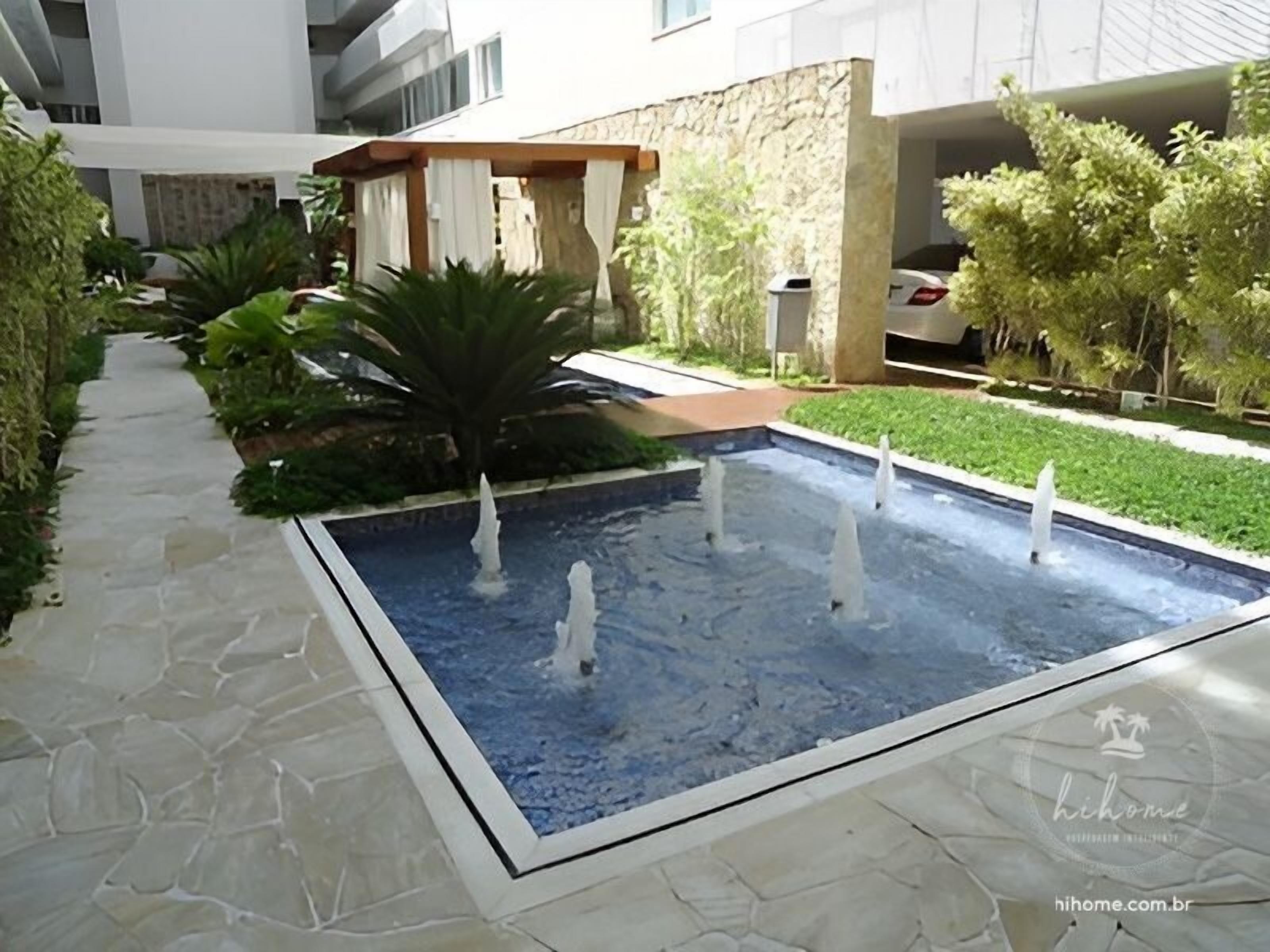 A swimming pool with multiple water jets, surrounded by a stone pathway and lush greenery.