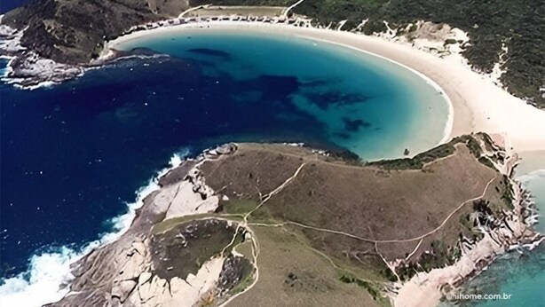 An aerial view of a coastal area with a curved beach, rocky terrain, and a road leading to the beach. - hihome – Mandai Flat (Cabo Frio)