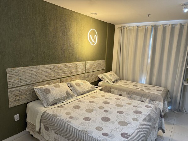 A hotel room with a brick-patterned headboard, two beds with patterned bedding, a wall-mounted light, and a window with curtains. - hihome – Mandai Flat (Cabo Frio)