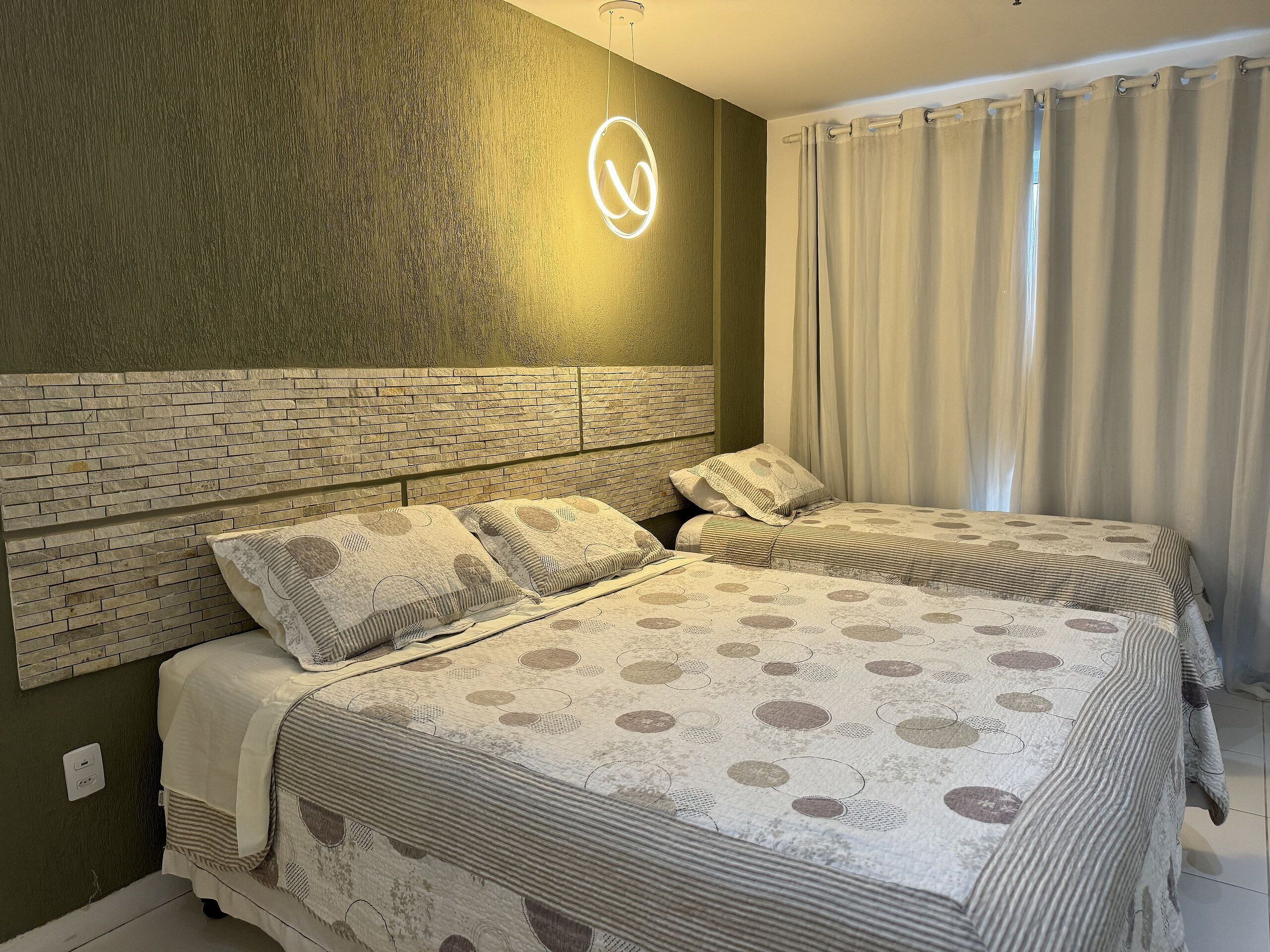 Un dormitorio con dos camas, cabecera de ladrillo y lámpara de techo circular.