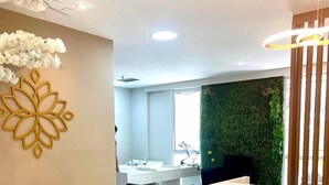 A modern reception area with a reception desk, two sofas, a desk with a computer, and a green wall. - hihome – Mandai Flat (Cabo Frio)