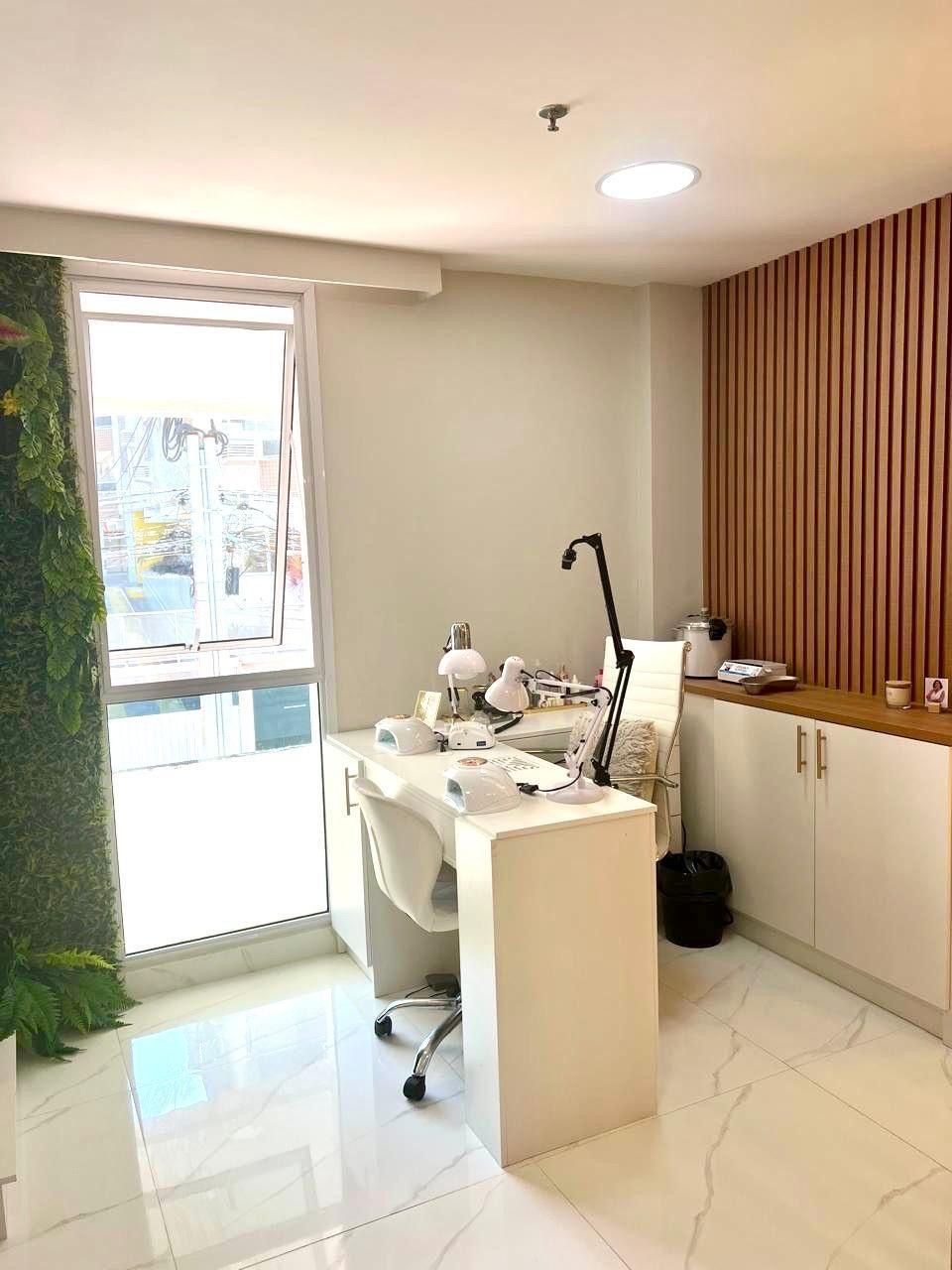 Ein modernes Büro mit weißem Schreibtisch, zwei Lampen und einem Computer. Ein Fenster mit Jalousien, eine Pflanze und eine Tür sind ebenfalls vorhanden.