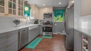 A modern kitchen with white cabinets, stainless steel appliances, and a window with teal curtains.