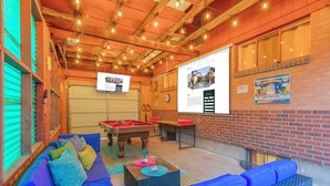 A pool area with a pool table, blue sofas, and a brick wall with a poster.