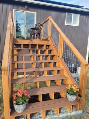 A wooden staircase with a metal railing leading to a door. There are two potted plants on the steps. - Bulson Creek 1 Bedroom Guest House Suite
(Mount Vernon)