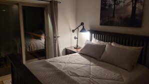 Une chambre à coucher comprenant un lit, une table de chevet, une lampe, un tableau et une porte-fenêtre coulissante donnant sur un balcon.