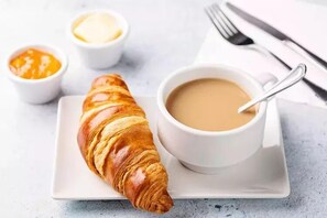 Un croissant sur une assiette blanche, accompagné d’une tasse de café et de deux petits ramequins de beurre.
