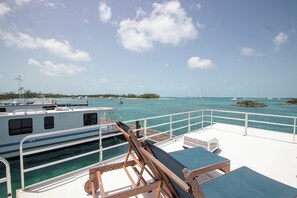 Un bateau doté d’un pont ensoleillé, de chaises longues et offrant une vue sur l’eau et les îles.