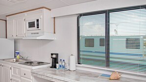 A kitchen with white cabinets, a microwave, a stove, and a window with blinds. - Aqua Village Resort (Stocking Island)