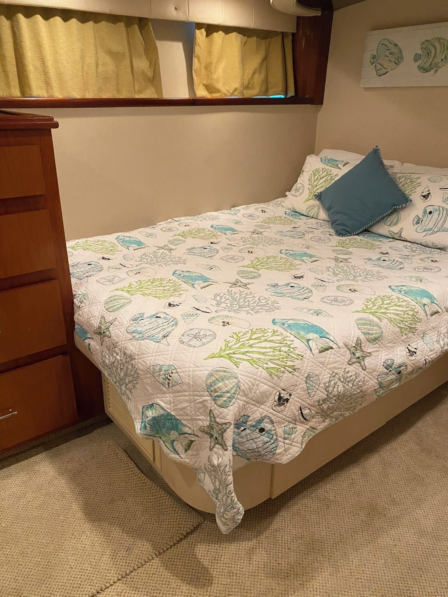 Un dormitorio con una cama adornada con colcha de motivos marinos, un aparador de madera y una ventana con cortinas.