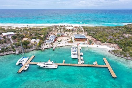 An aerial view of a coastal resort with a marina, clear turquoise waters, and a sandy beach.